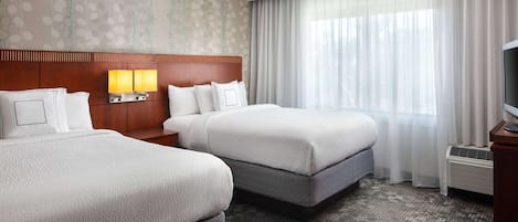A hotel room with two beds, a wooden headboard, a flat-screen TV, and a large window with sheer curtains.