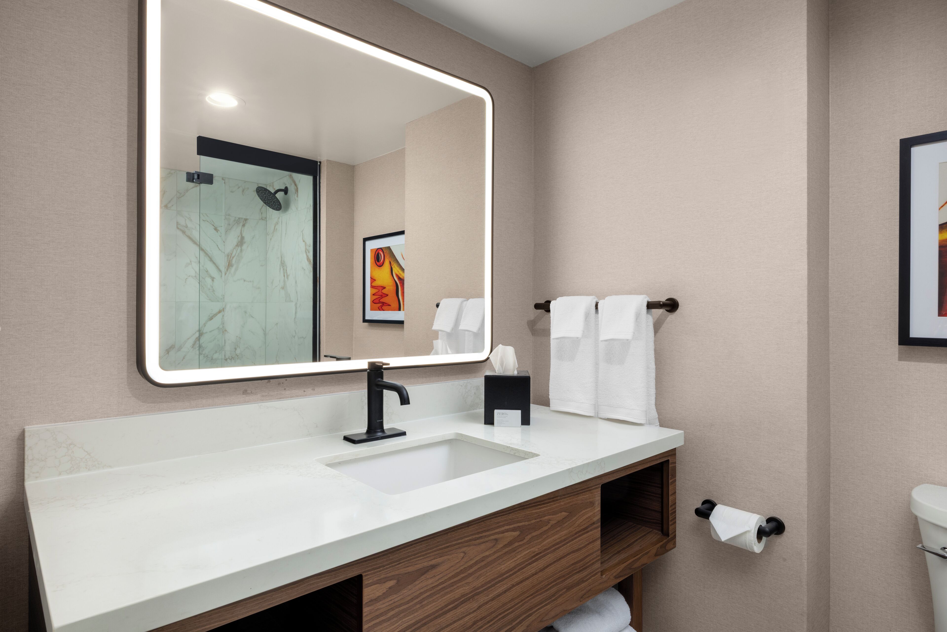 A modern bathroom with a large mirror, white sink, and wooden vanity.