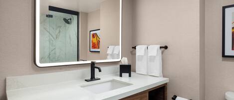 A modern bathroom with a large mirror, white sink, and wooden vanity.