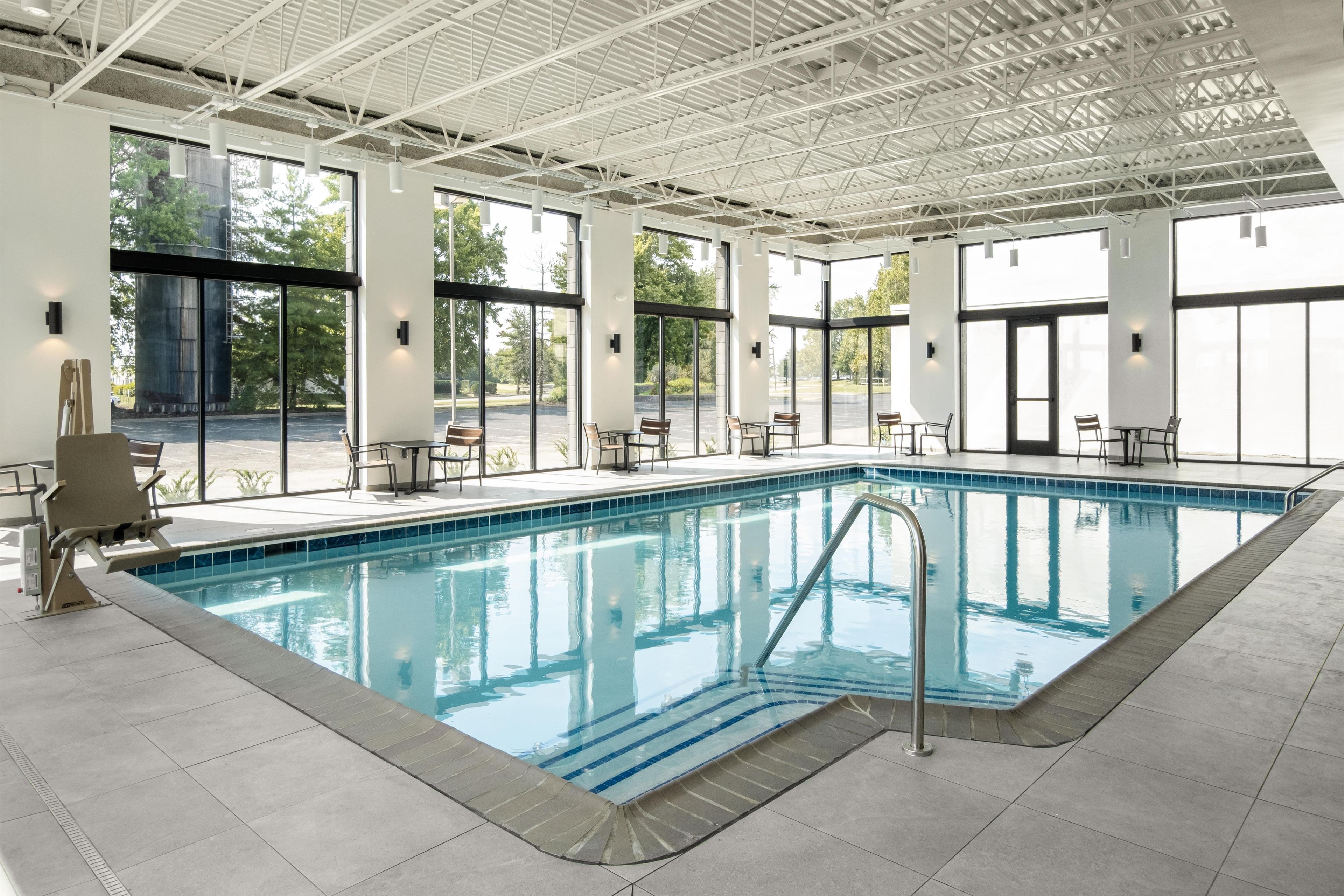 Una piscina interior con paredes de vidrio transparente, suelo de baldosas y varias zonas de estar alrededor.