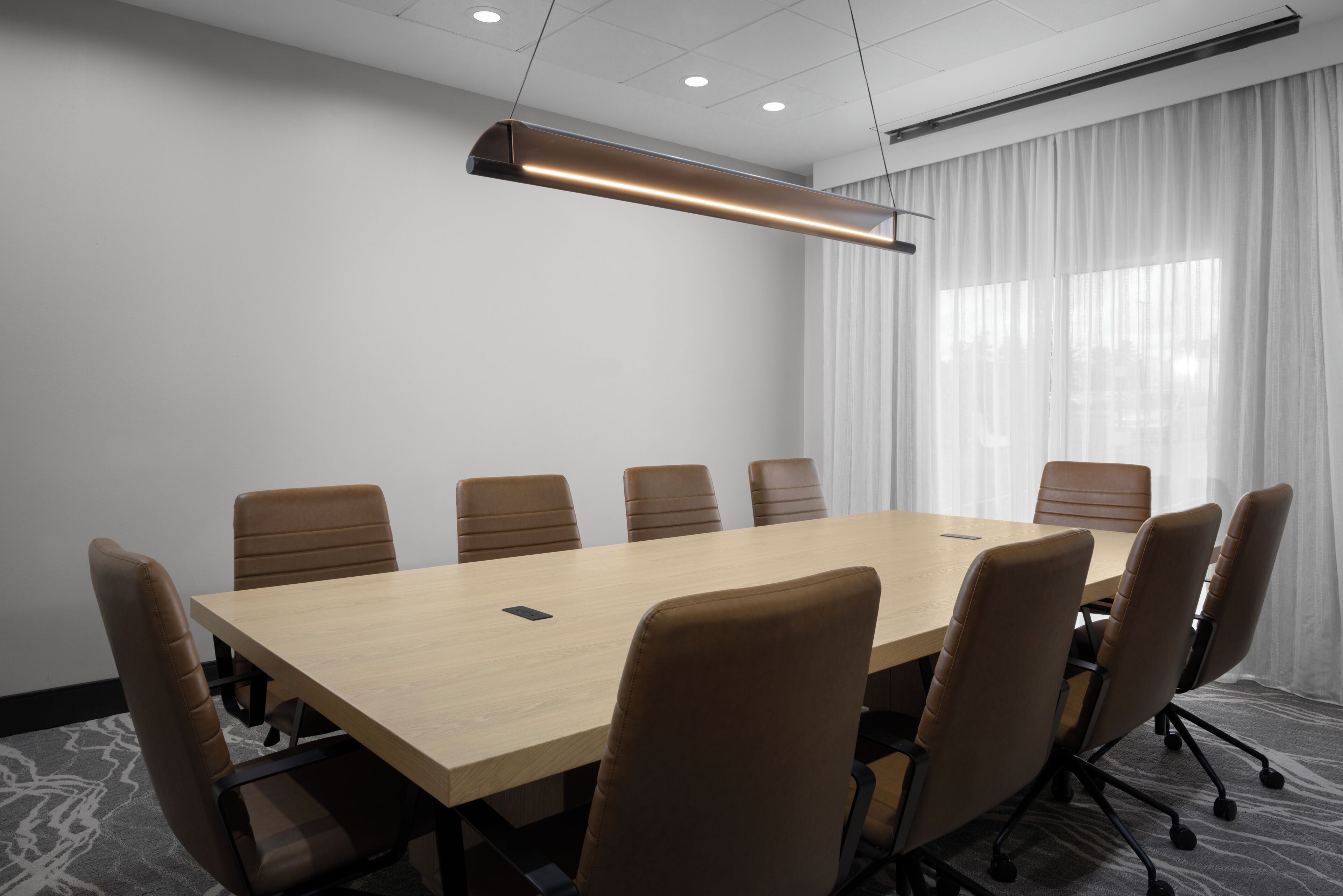 A conference room with a long table, six chairs, and a modern pendant light.