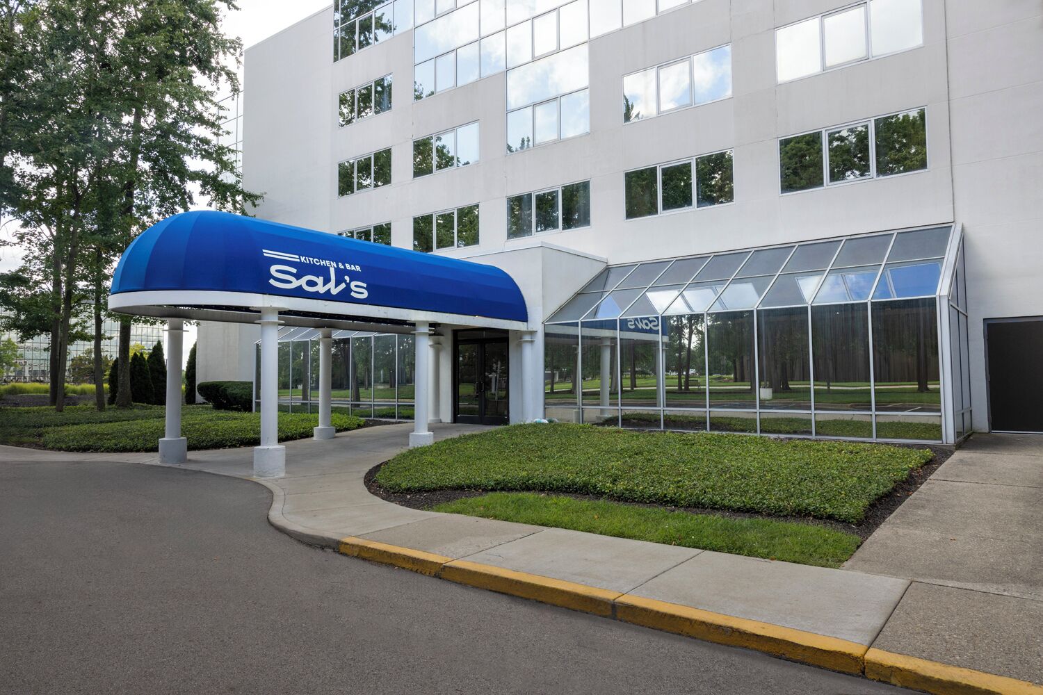 Un edificio moderno con un acceso cubierto identificado como 'Sal's' y una zona con cerramientos de vidrio.