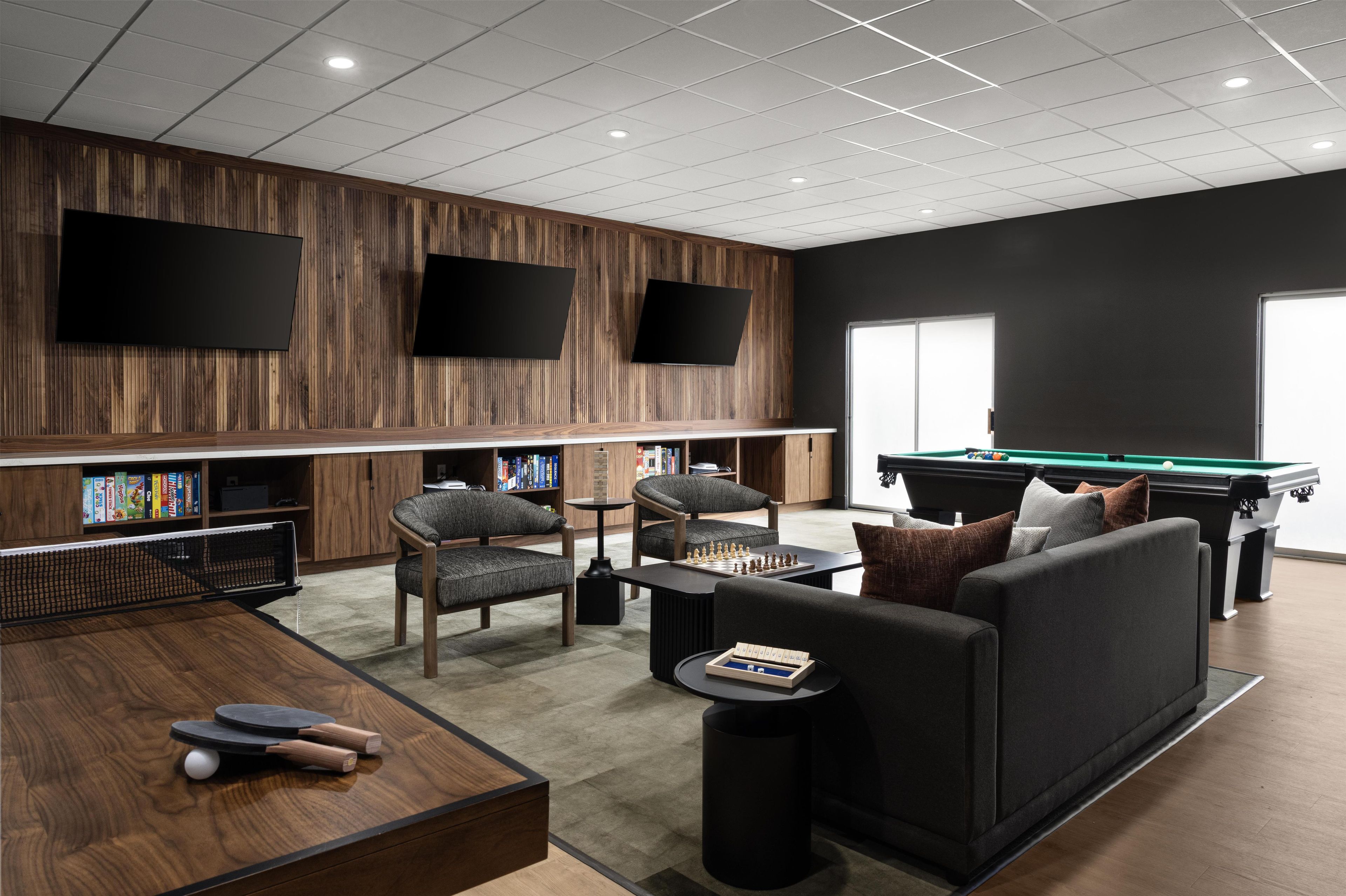 A modern lounge area with a pool table, comfortable seating, and a bookshelf.