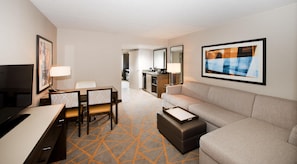 A hotel room with a dining area, a sofa, a TV, and a kitchen in the background. - Embassy Suites by Hilton Cincinnati Northeast Blue Ash (Cincinnati)