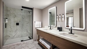 A modern bathroom with a glass shower enclosure, a vanity with two sinks, and a large mirror. - Embassy Suites by Hilton Cincinnati Northeast Blue Ash (Cincinnati)