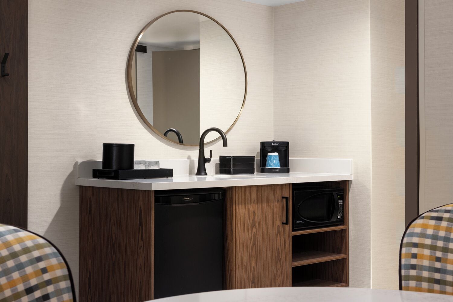 Un baño moderno con un espejo redondo, grifo negro, cafetera y lavavajillas integrado.