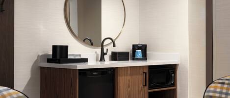 Un baño moderno con un espejo redondo, grifo negro, cafetera y lavavajillas integrado.