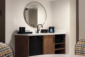 A modern bathroom with a round mirror, black faucet, coffee machine, and built-in dishwasher. - Embassy Suites by Hilton Cincinnati Northeast Blue Ash (Cincinnati)