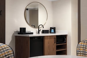 Un baño moderno con un espejo redondo, grifo negro, cafetera y lavavajillas integrado.