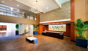 A spacious lobby with a reception desk, wooden flooring, and multiple potted plants.