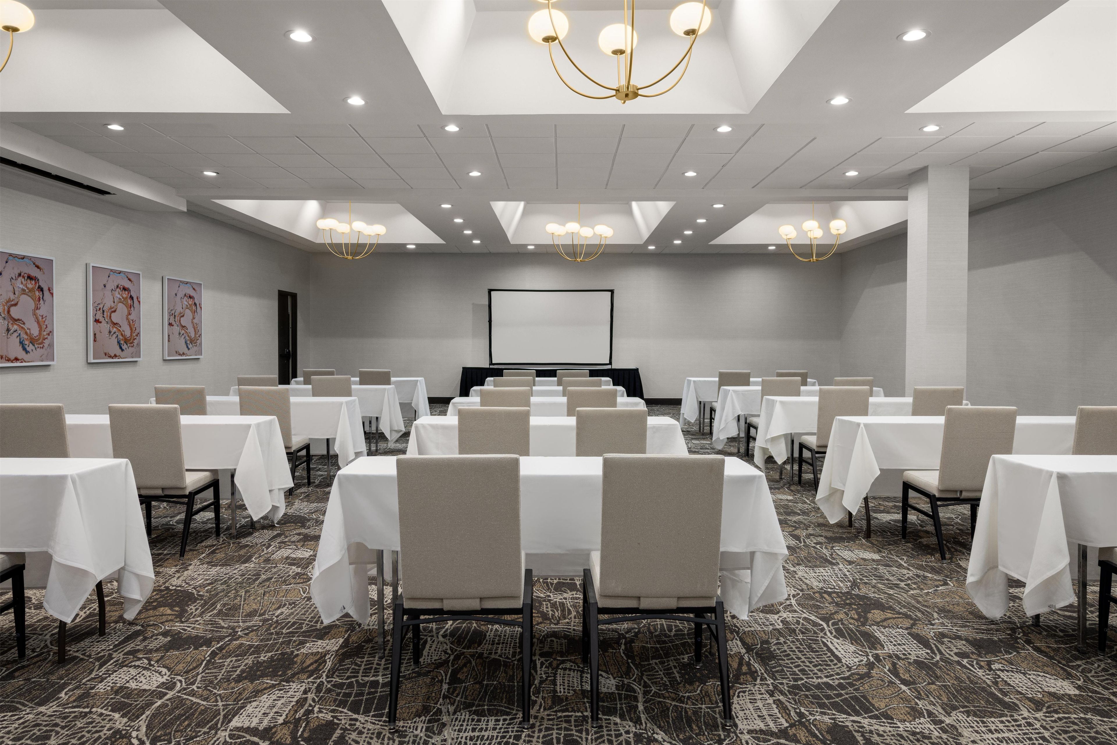 A conference room with multiple tables and chairs, a large screen, and a patterned carpet.