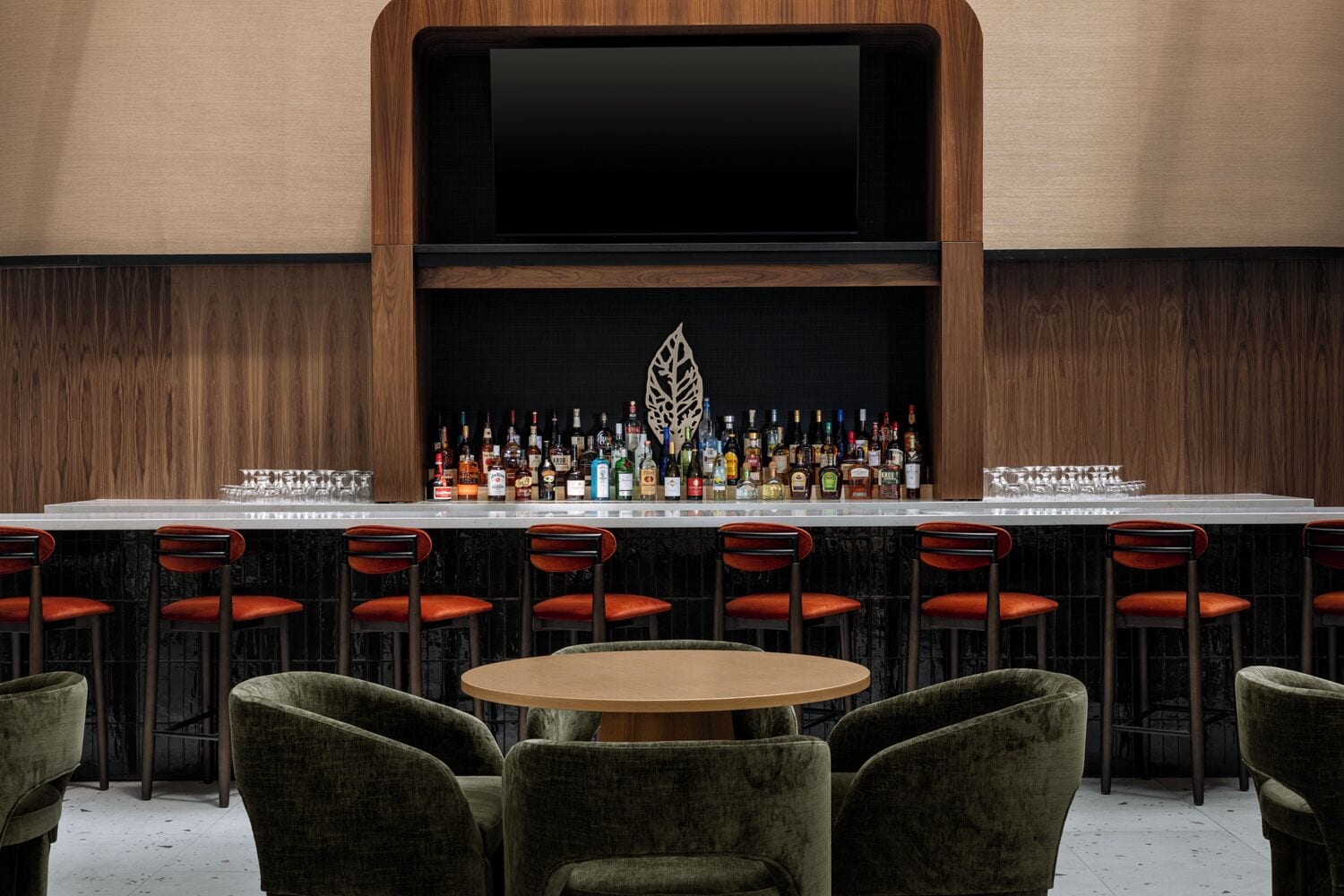 Una zona de bar con una barra larga, varios taburetes y una mesa redonda.