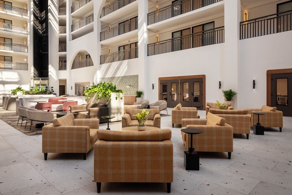A spacious lobby with multiple seating areas, a central plant, and a high ceiling with balconies. - Embassy Suites by Hilton Cincinnati Northeast Blue Ash (Cincinnati)