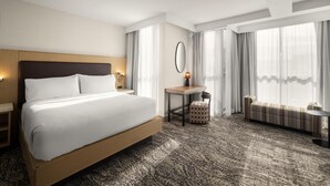 Una camera d'albergo con un letto grande, un tavolino, un divano e un'ampia finestra con tende.