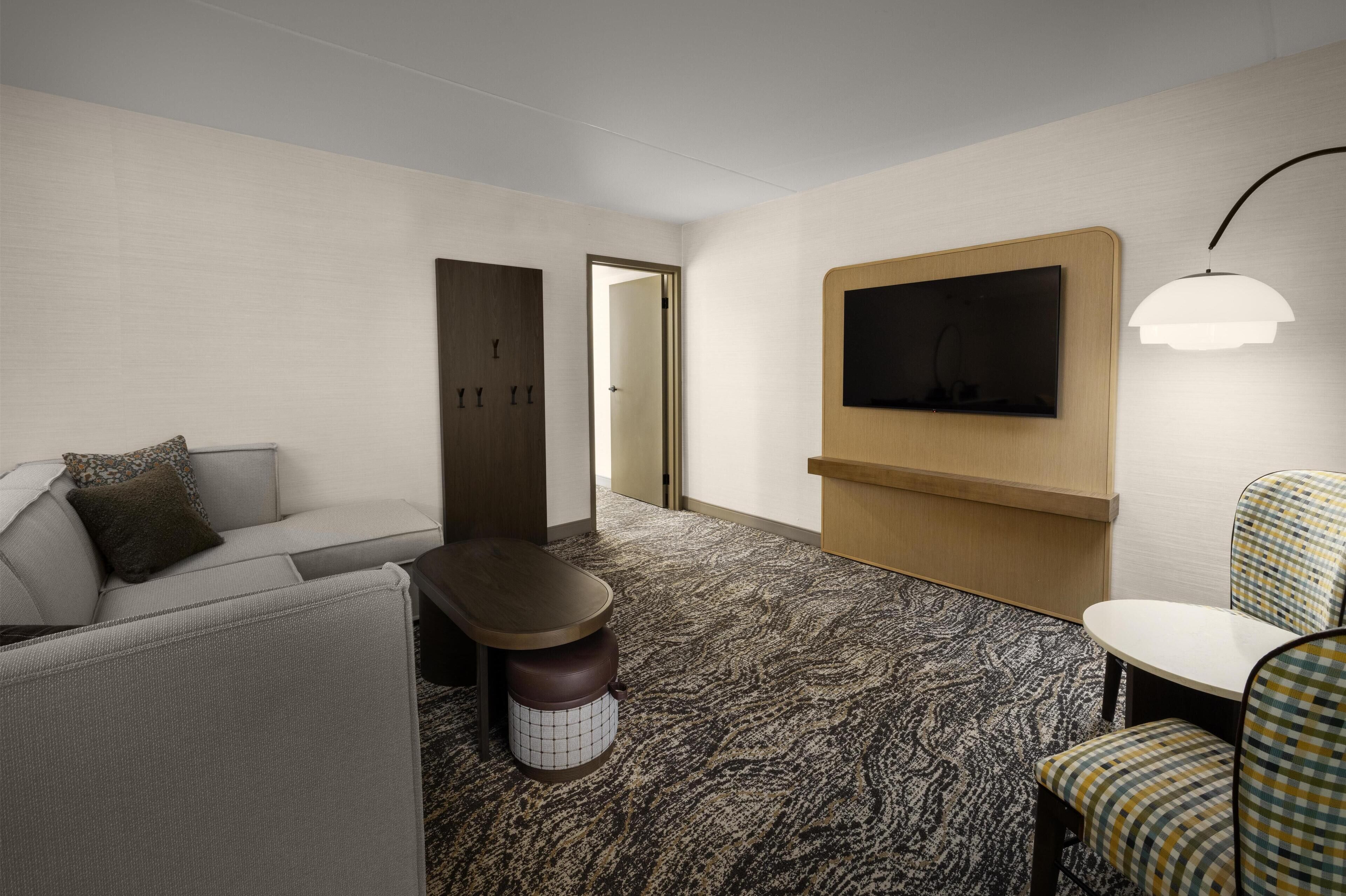 Une chambre d’hôtel avec un canapé, une petite table, un téléviseur fixé au mur et une moquette à motifs.