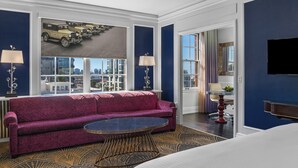 A hotel room with a large window, a purple sofa, a round coffee table, and a flat-screen TV. - Inn At The Park (San Diego)