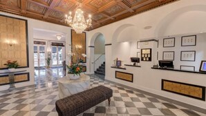 A lobby with a checkered floor, a marble bench, a chandelier, and framed pictures on the walls. - Inn At The Park (San Diego)