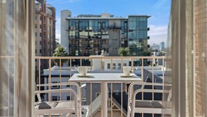 A balcony with two white tables and chairs, overlooking a cityscape with modern buildings. - Inn At The Park (San Diego)