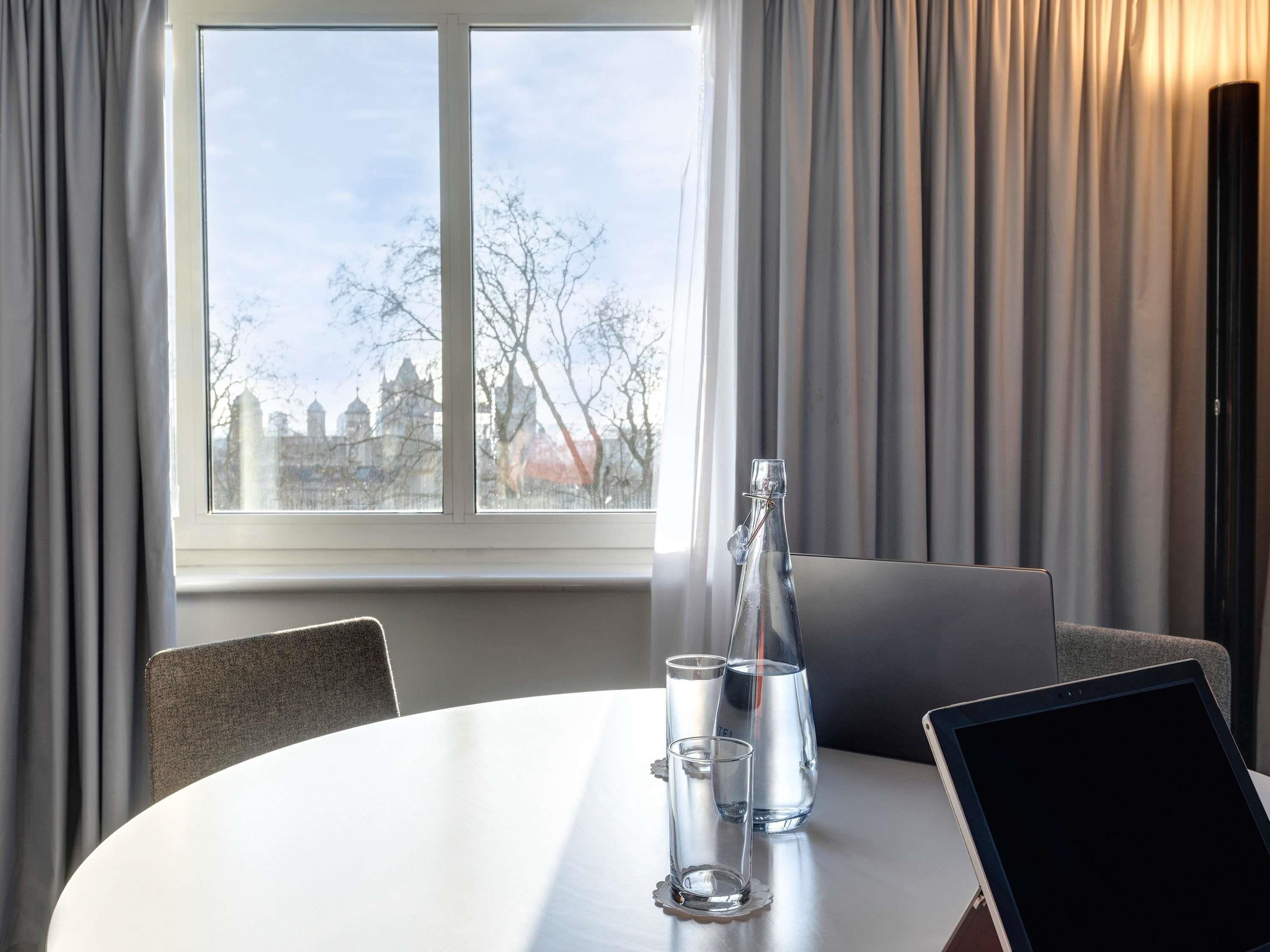 Een hotelkamer met een ronde tafel, een laptop, een fles en glazen.