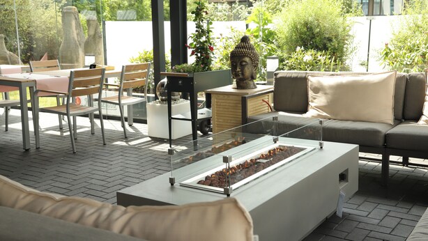 An outdoor seating area with tables, chairs, a Buddha statue, and a fire feature. - Fora Hotel Hannover by Mercure (Hannover)