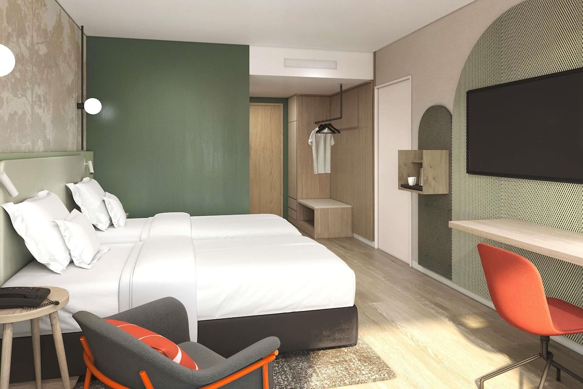 A modern hotel room with a bed, desk, chair, and a TV.