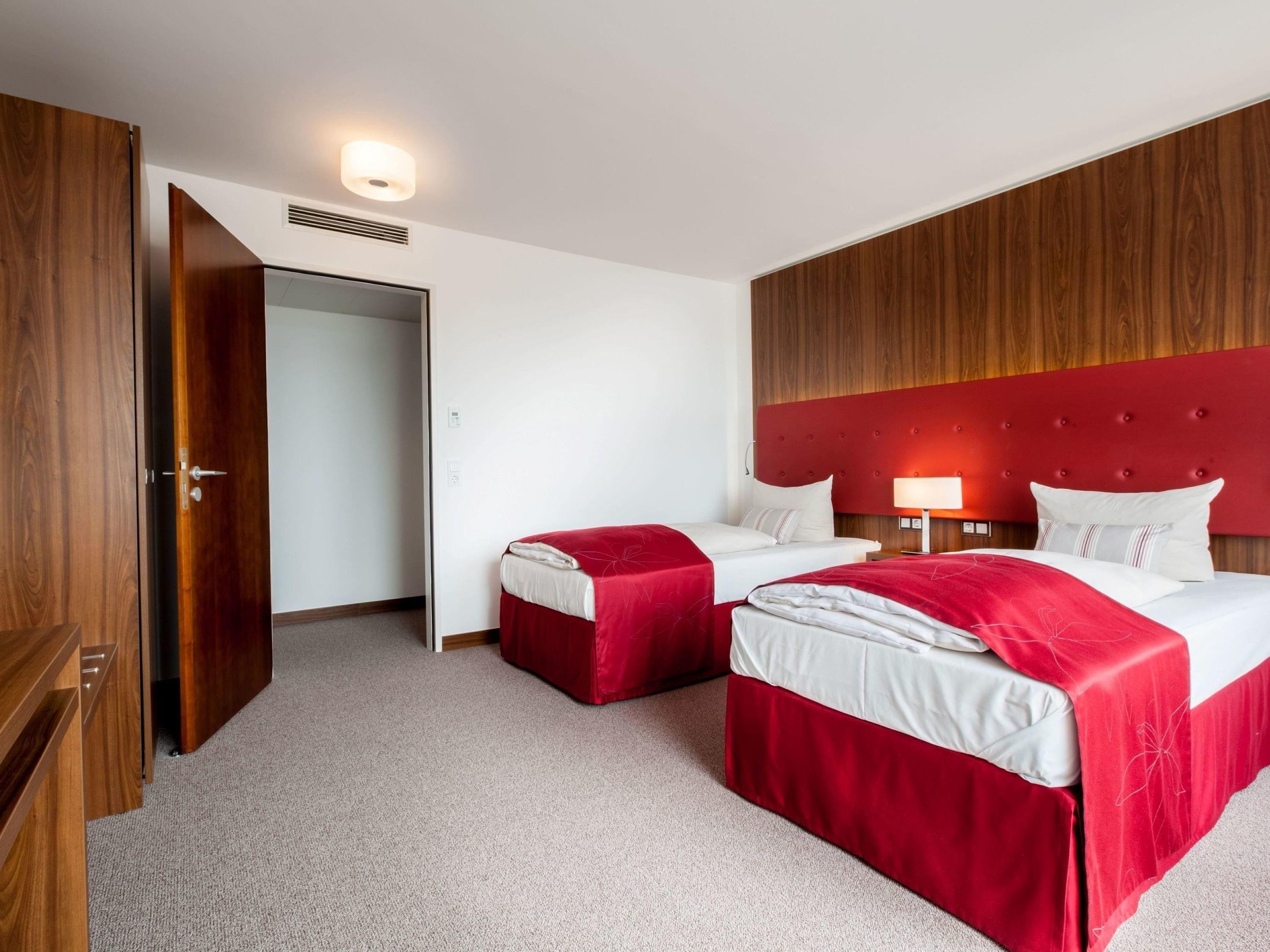 Ein Hotelzimmer mit zwei Betten, einem Holzschrank, einem roten Kopfteil und einer Nachttischlampe.