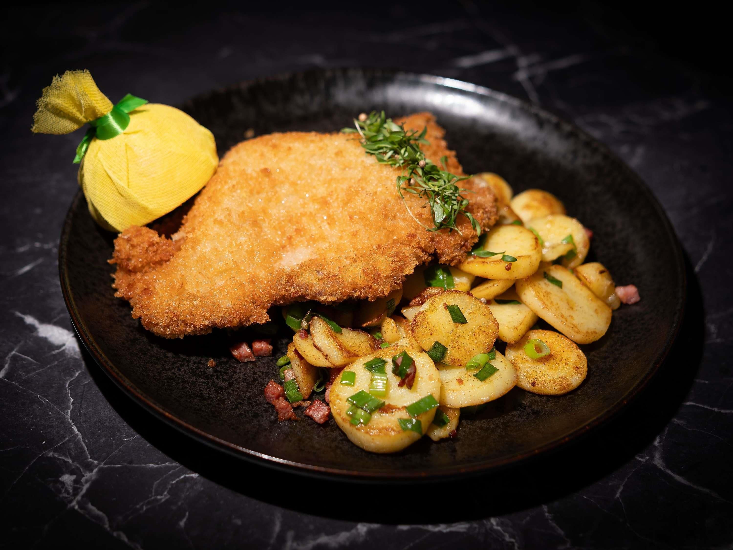 Ein Teller mit einem panierten Schnitzel, Kartoffelscheiben und einem Zitronenschnitz.