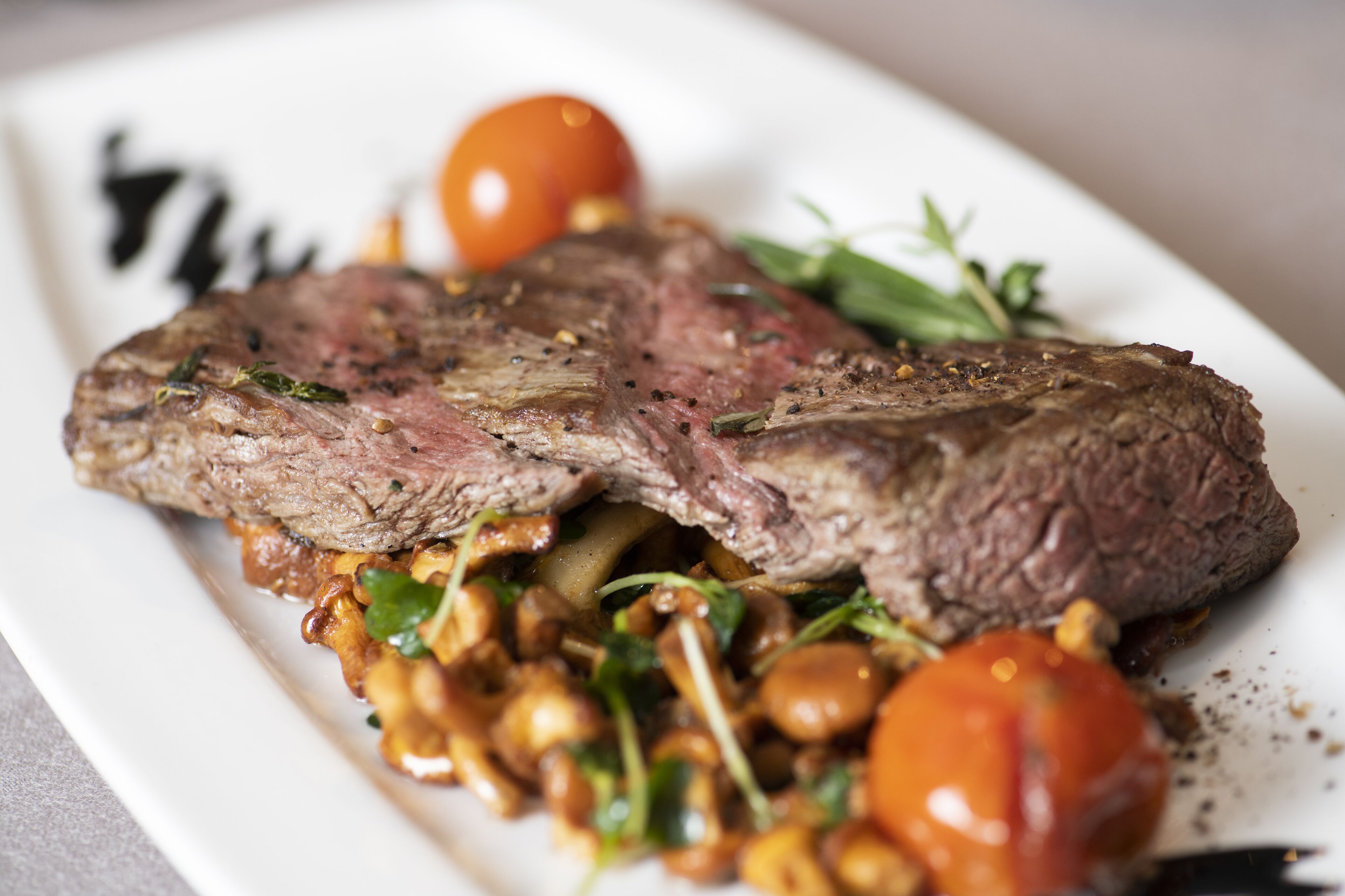 A plate of steak with vegetables and a cherry tomato.