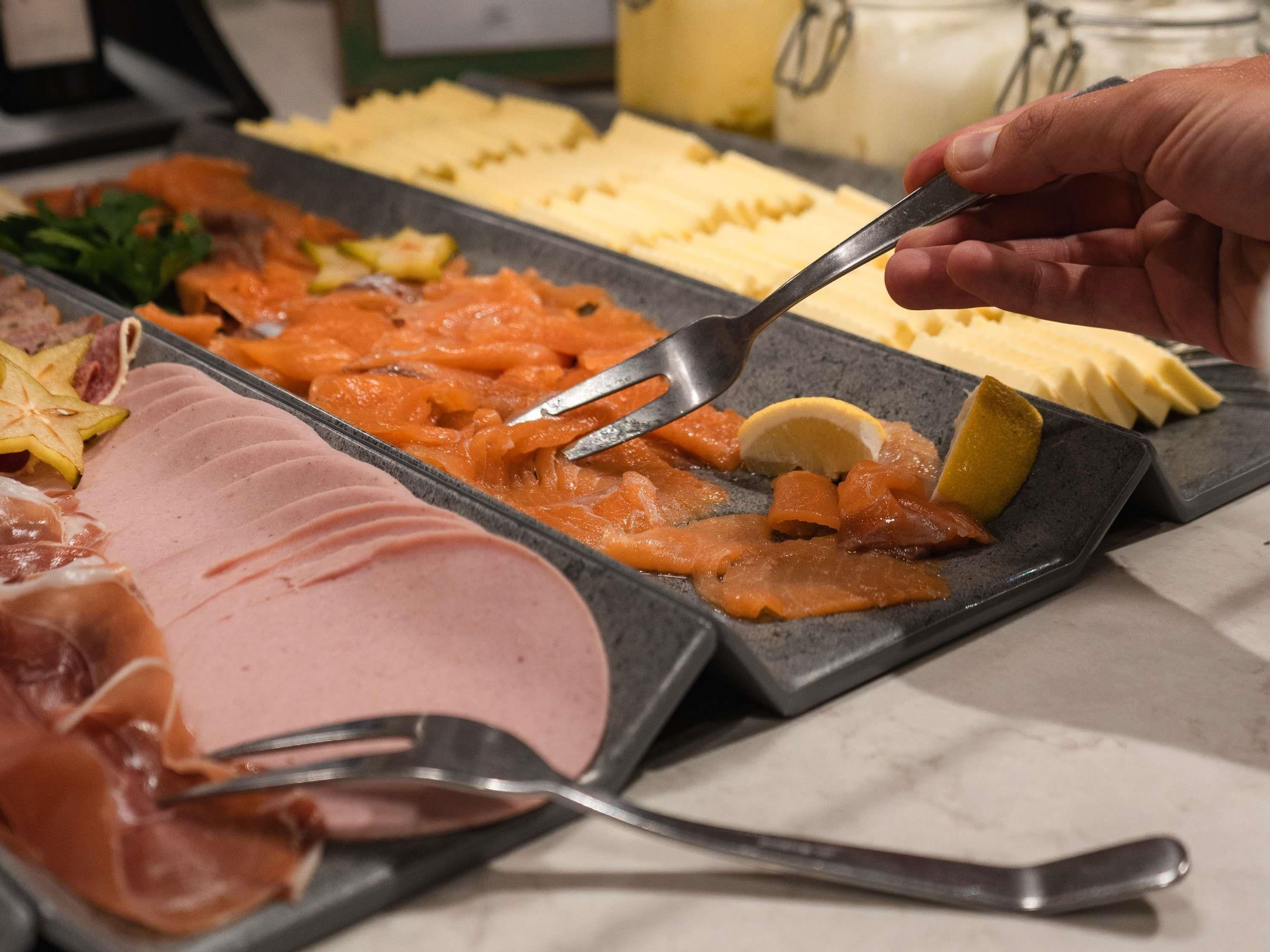Un bufé con diversas opciones de comida, incluyendo carnes cortadas y un plato con salsa cremosa.