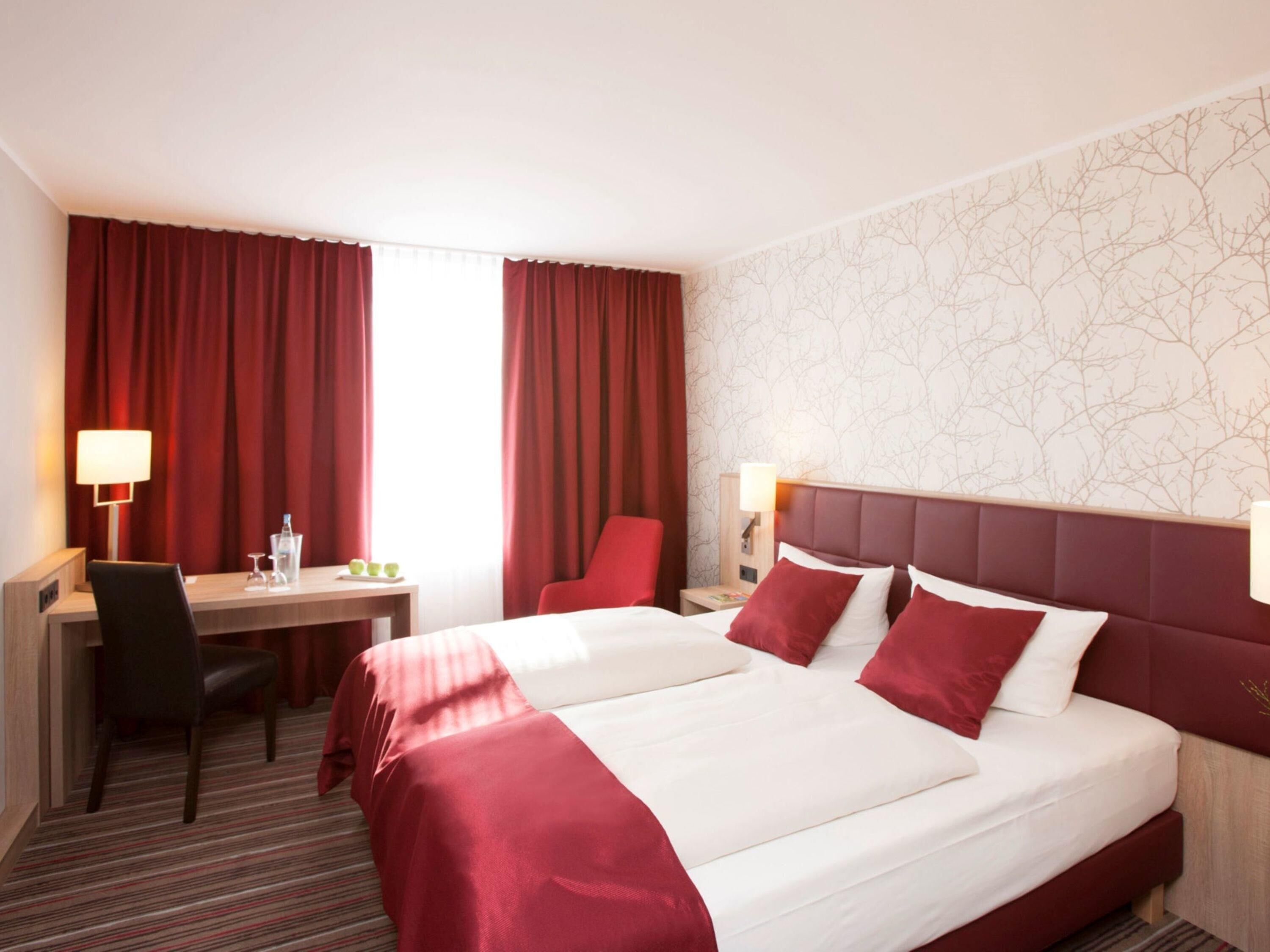 A hotel room with a bed, desk, chair, and two bedside lamps.