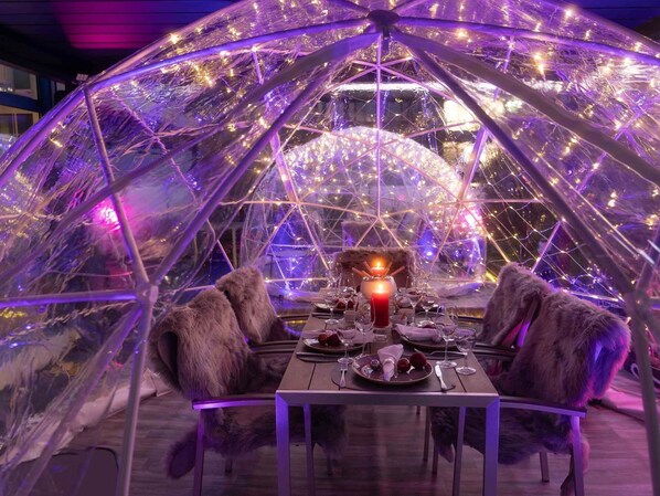 Comedor con una mesa dispuesta para cuatro, rodeado por una estructura de cúpula geométrica con iluminación interior.