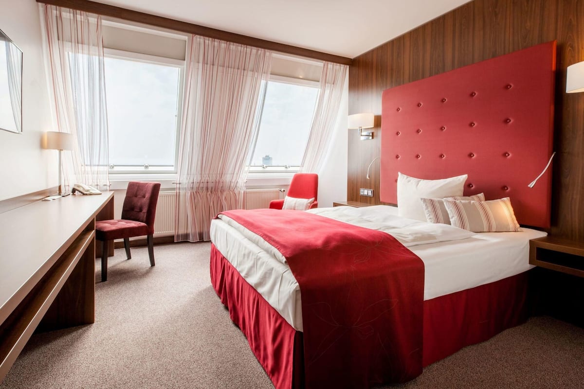 A hotel room with a large bed, a desk, a chair, and a window with curtains.