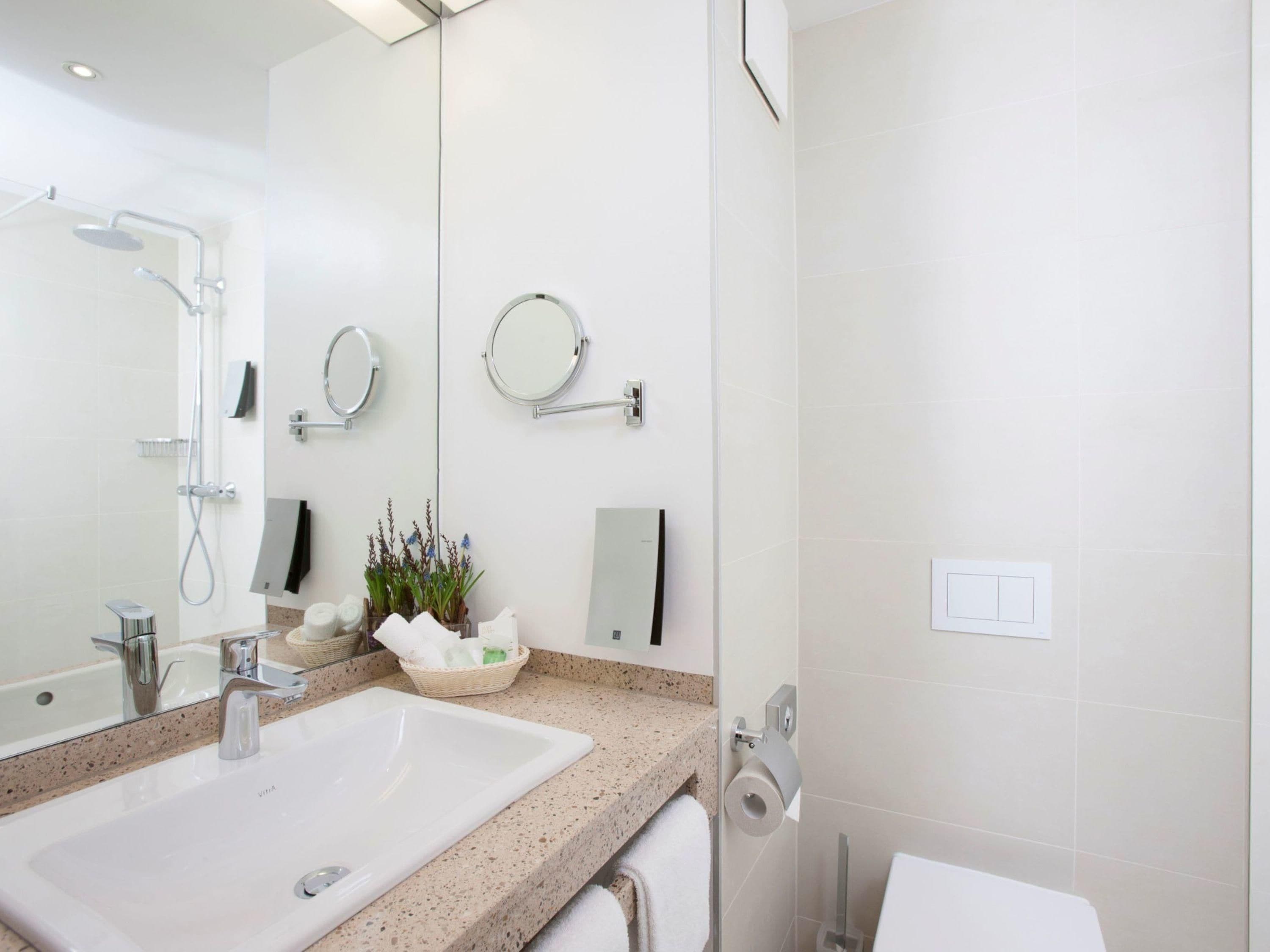 Un baño moderno con lavamanos, espejo, toallero y ducha.