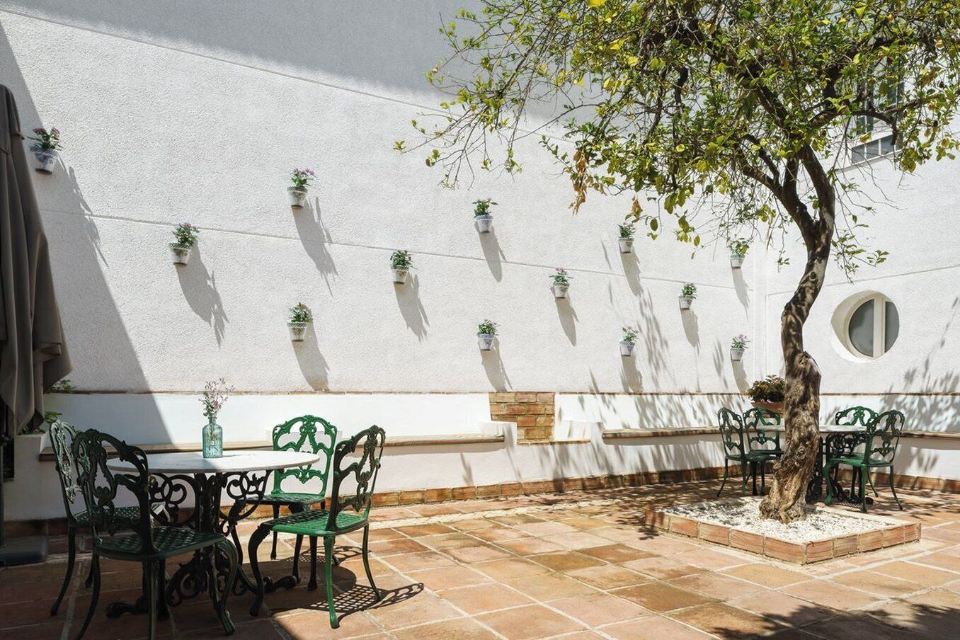 Un patio al aire libre con pared blanca, sillas verdes y plantas en macetas.