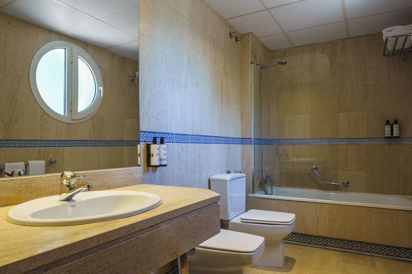 Ein Badezimmer mit rundem Spiegel, Waschbecken, Toilette und Duschbereich.