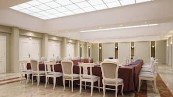 Un salón de conferencias con una larga mesa, sillas blancas y un techo alto con tragaluces.