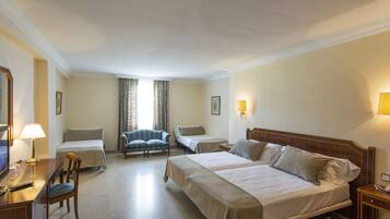A hotel room with two beds, a desk with a lamp, a chair, and a TV.
