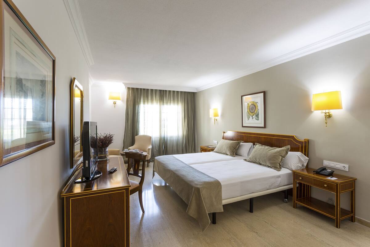 Een hotelkamer met een groot bed, een bureau met een computer, een stoel en twee nachtkastjes met lampen.