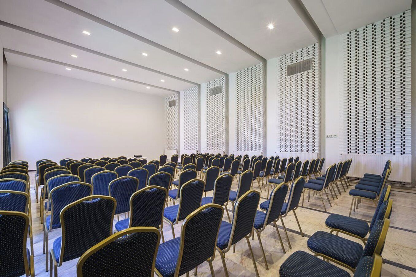 Une salle de conférence avec des rangées de chaises bleues et un plafond blanc doté d’un éclairage encastré.