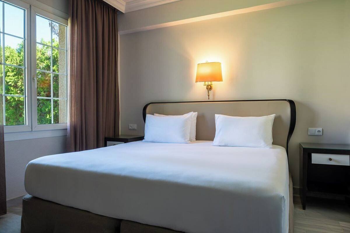 Een hotelkamer met een groot bed, twee nachtkastjes, een lamp en een raam met gordijnen.