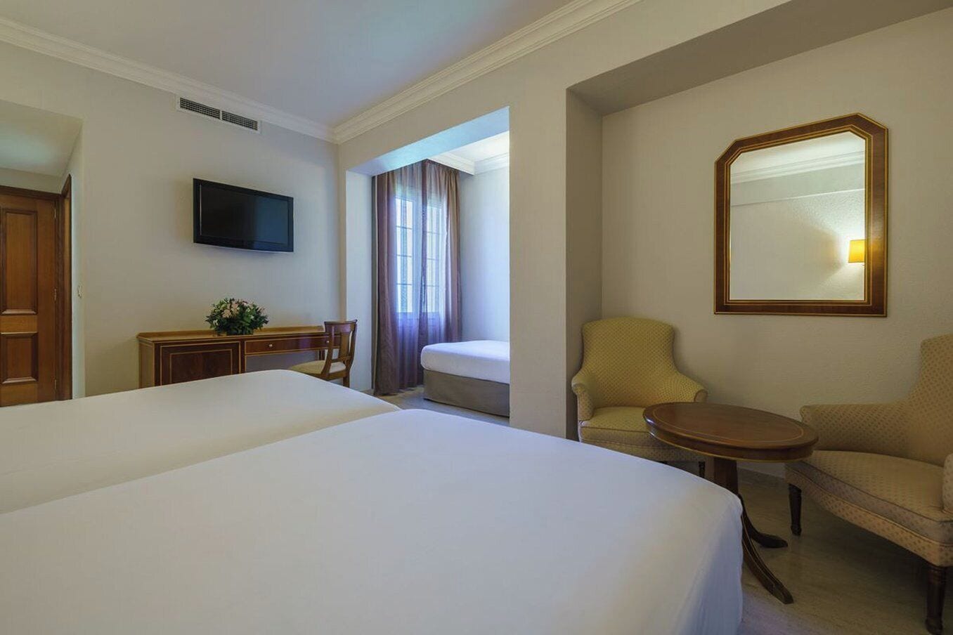 Habitación de hotel con una cama grande, un escritorio con silla, una mesita redonda pequeña, un sofá y un televisor montado en la pared.