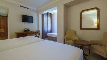 Habitación de hotel con una cama grande, un escritorio con silla, una mesita redonda pequeña, un sofá y un televisor montado en la pared.