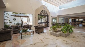 Un vestíbulo espacioso con techo alto, zona de estar con sofás y una mesa de centro, y un gran ventanal con vistas a un patio.