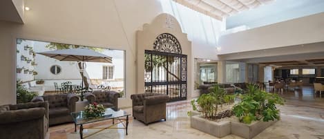 Un vestíbulo espacioso con techo alto, zona de estar con sofás y una mesa de centro, y un gran ventanal con vistas a un patio.