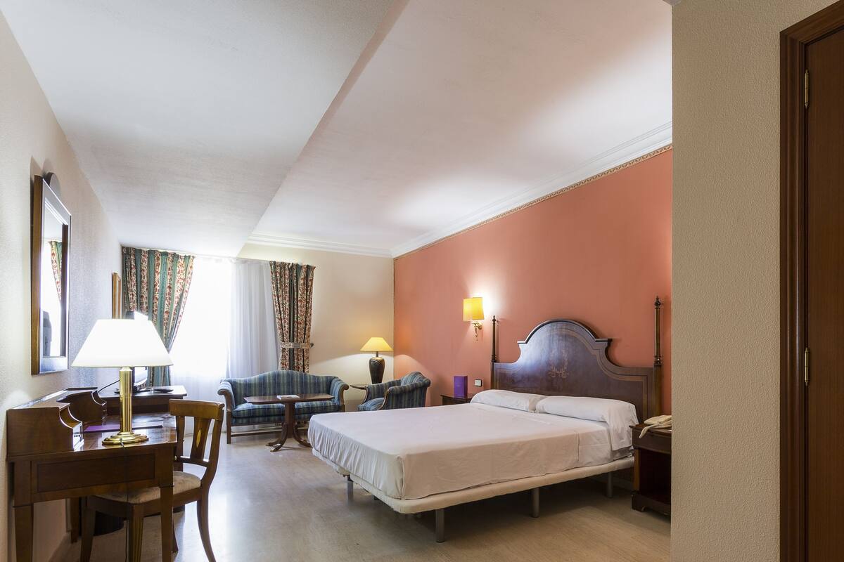 Een hotelkamer met een bed, bureau, stoel en twee lampen.