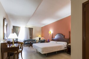 A hotel room with a bed, desk, chair, and two lamps.