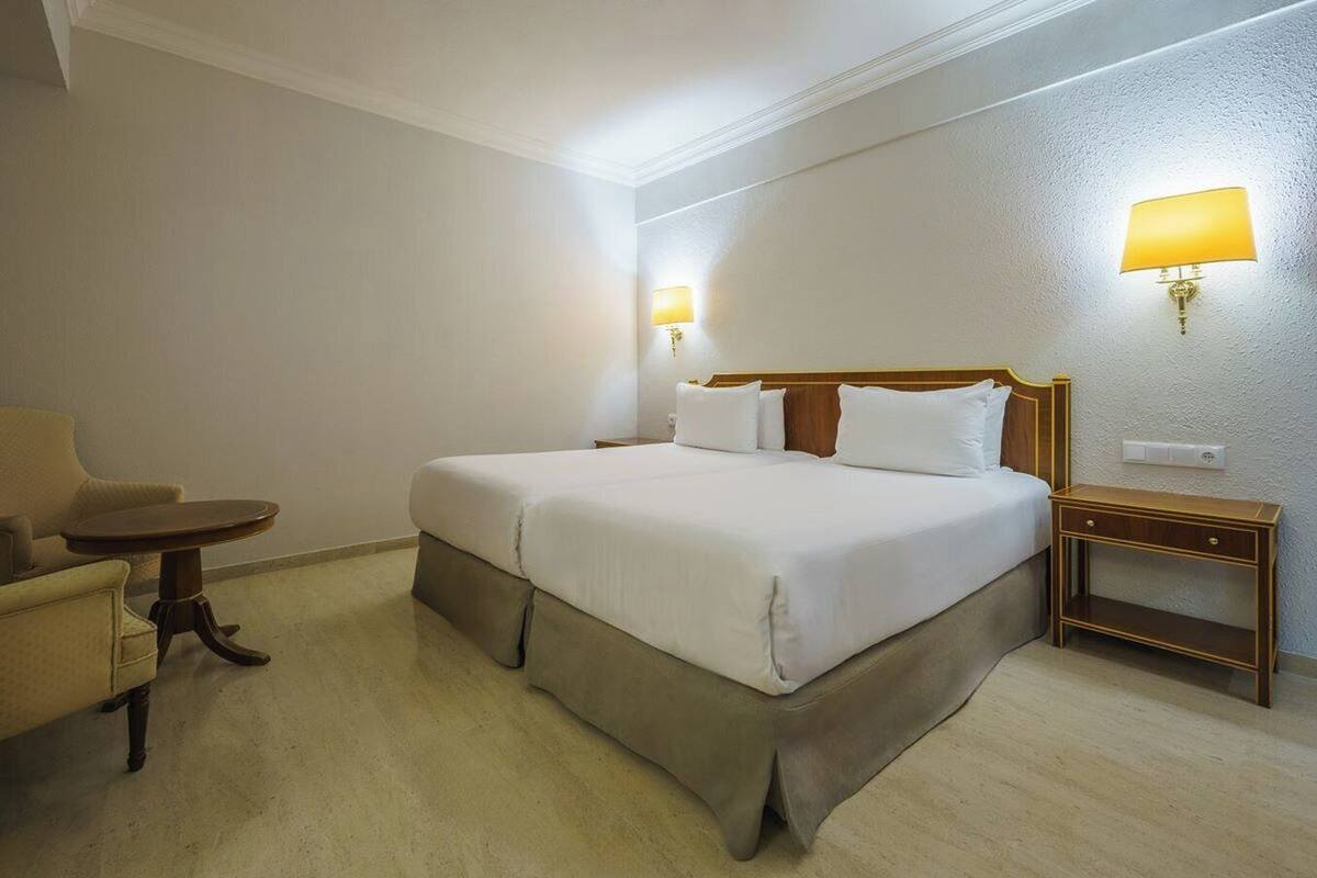 Een hotelkamer met een bed, nachtkastje, lamp en een stoel.