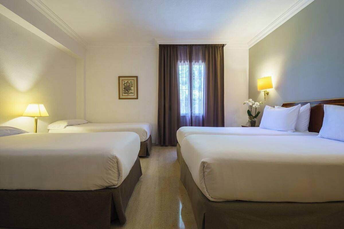 Hotelkamer met twee bedden, een nachtkastje met lamp, een lijst aan de muur en een raam met gordijnen.