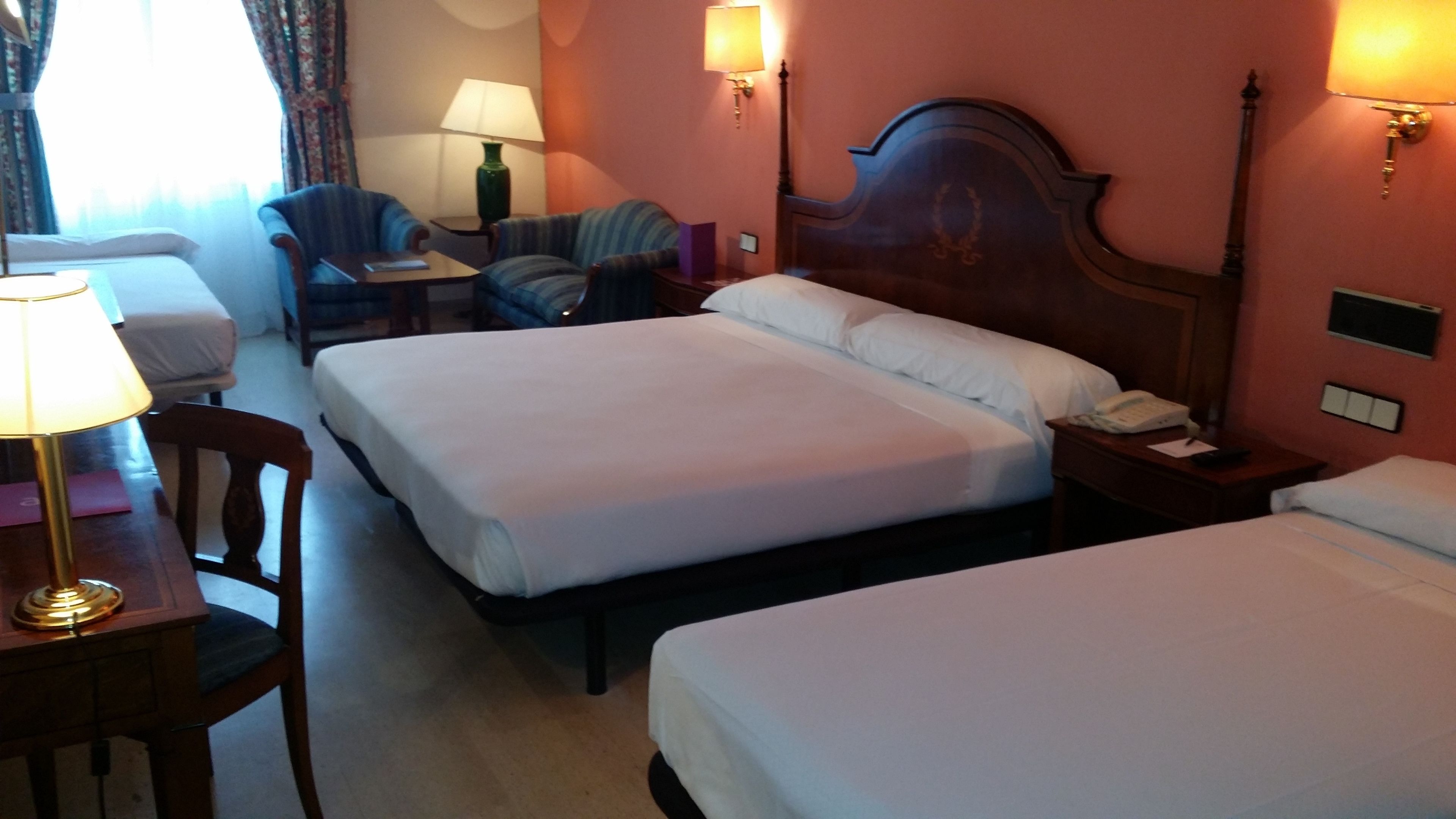 Habitación de hotel con dos camas, un escritorio con lámpara, una silla y una mesita de noche con teléfono.