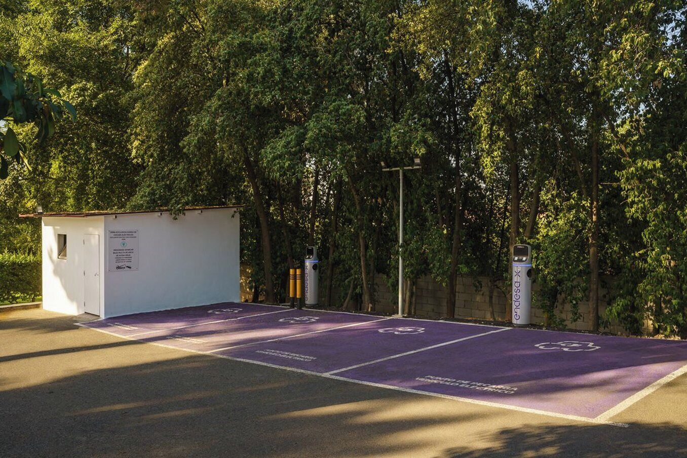 A parking area with a small white building, a trash bin, and a sign with a logo.
